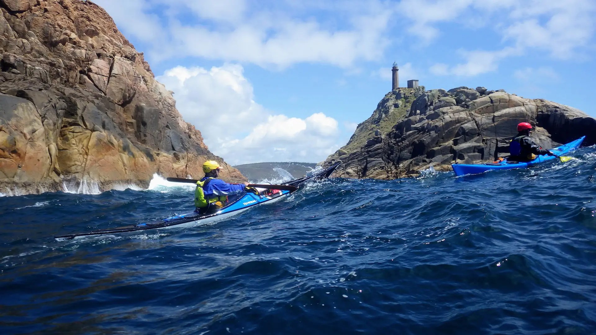 Dos palistas en kayak de mar navegando frente a un faro en formación oficial ACA