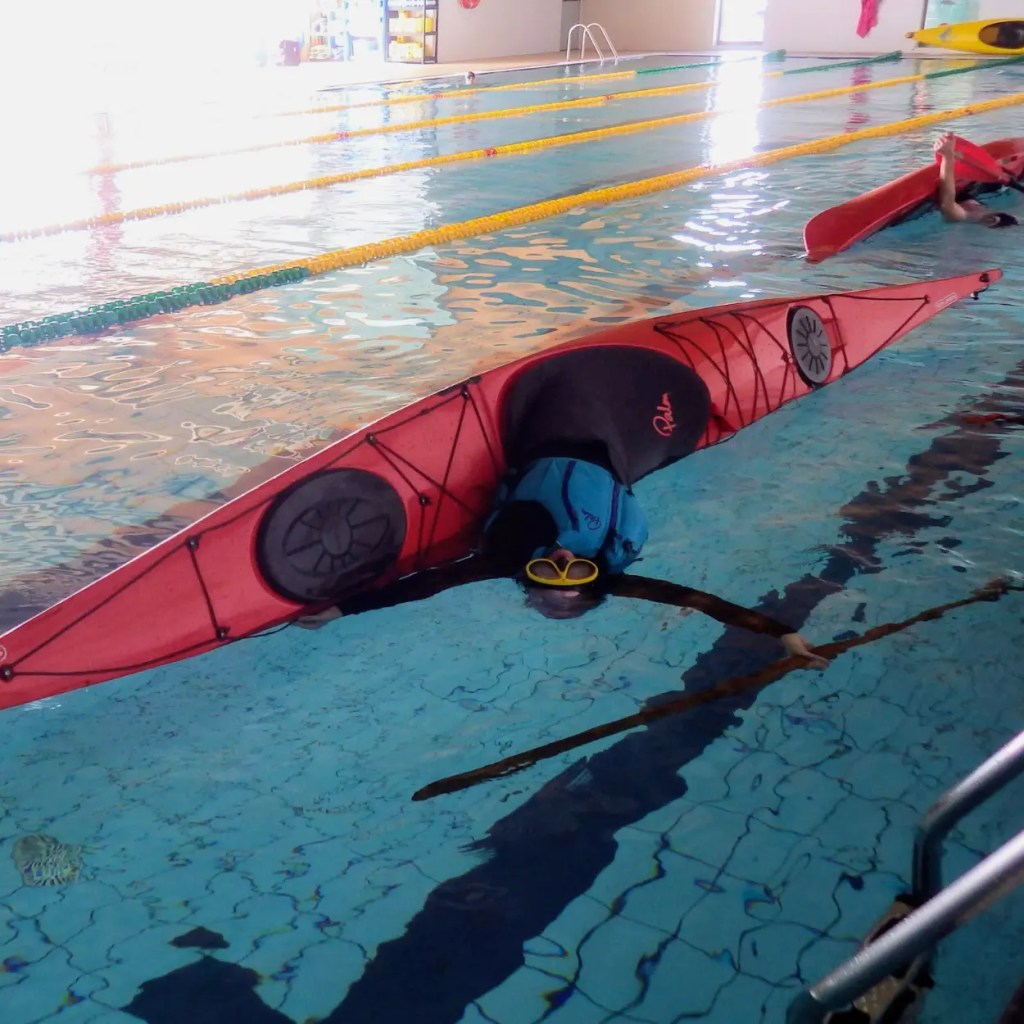 Palista practicando la maniobra de esquimotaje (Eskimo Roll) en una piscina climatizada bajo supervisión técnica