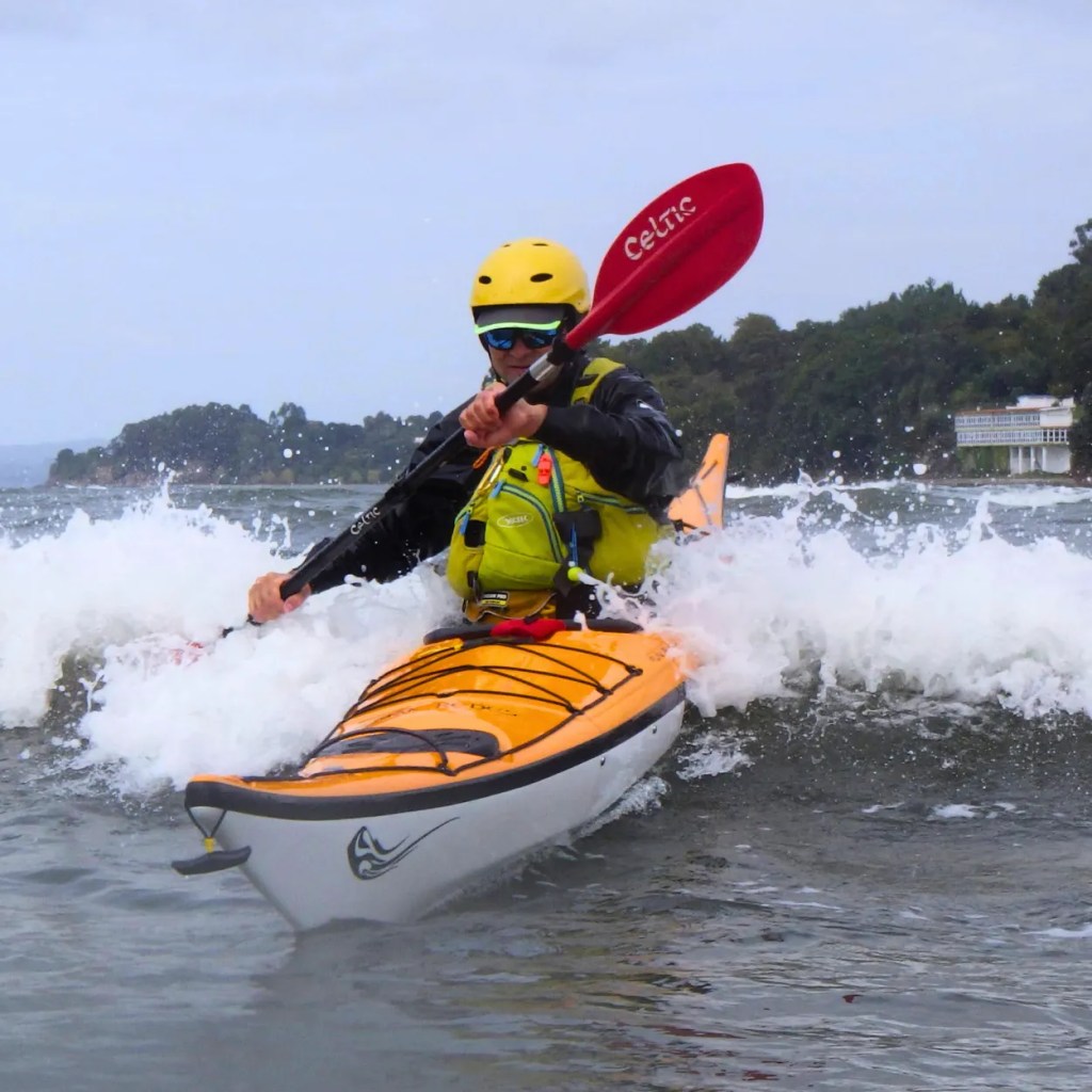 Palista en kayak de mar navegando entre olas y rompientes cerca de acantilados".