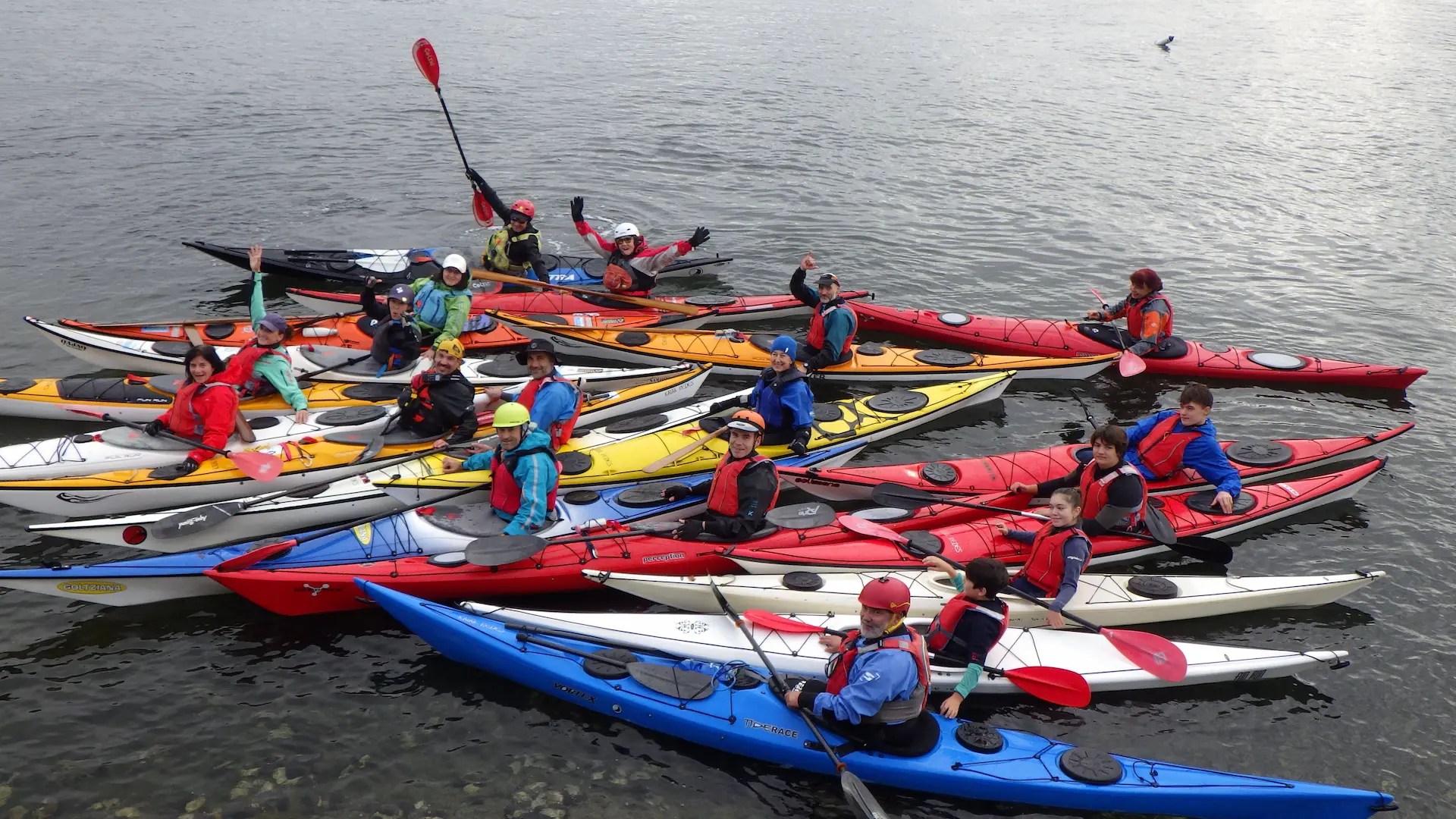 Grupo numeroso de hombres y mujeres del club Kayak Redes posando juntos en sus coloridos kayaks sobre el agua.
