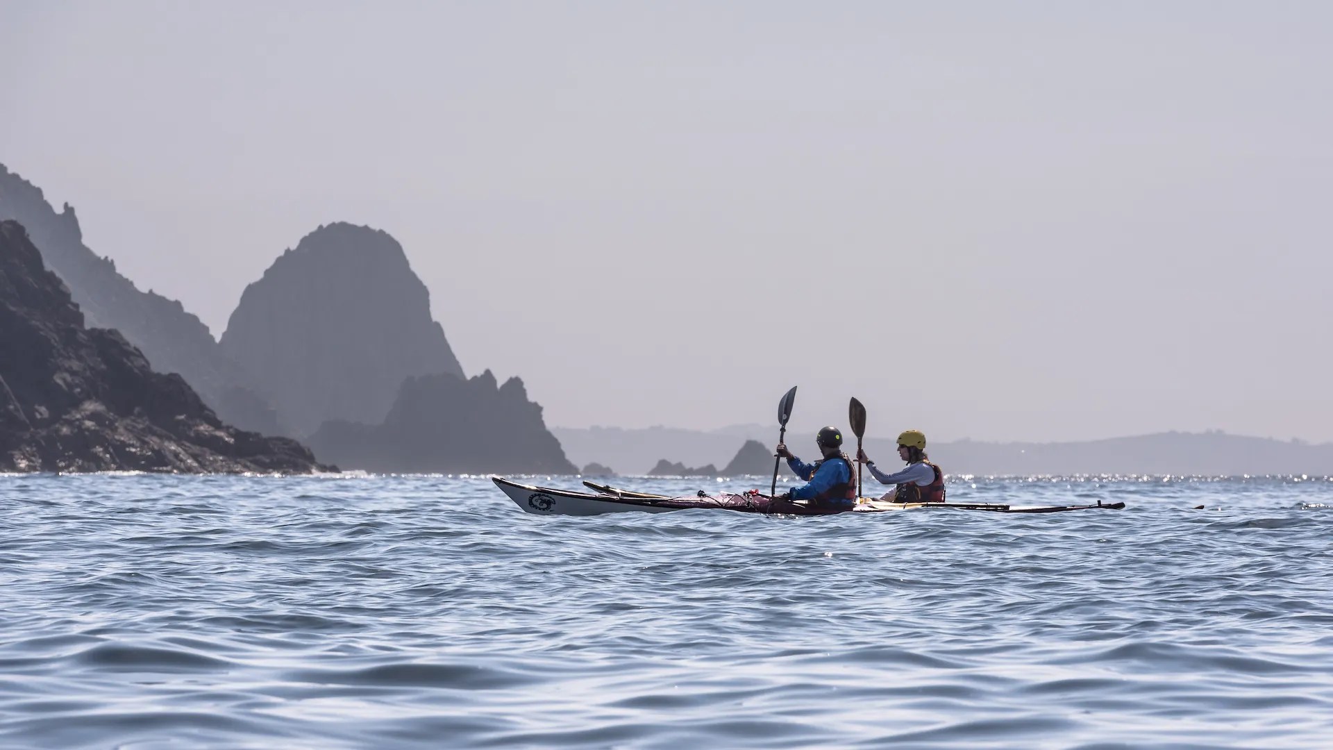 Dos kayakistas navegando cerca de acantilados rocosos en la costa de Galicia.